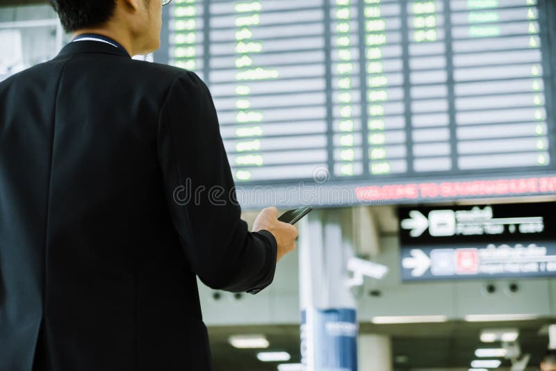 Elegant asian businessman checking email on mobile phone while walking with suitcase inside airport, experienced male employer using cell telephone while waiting for taxi car coming before work travel