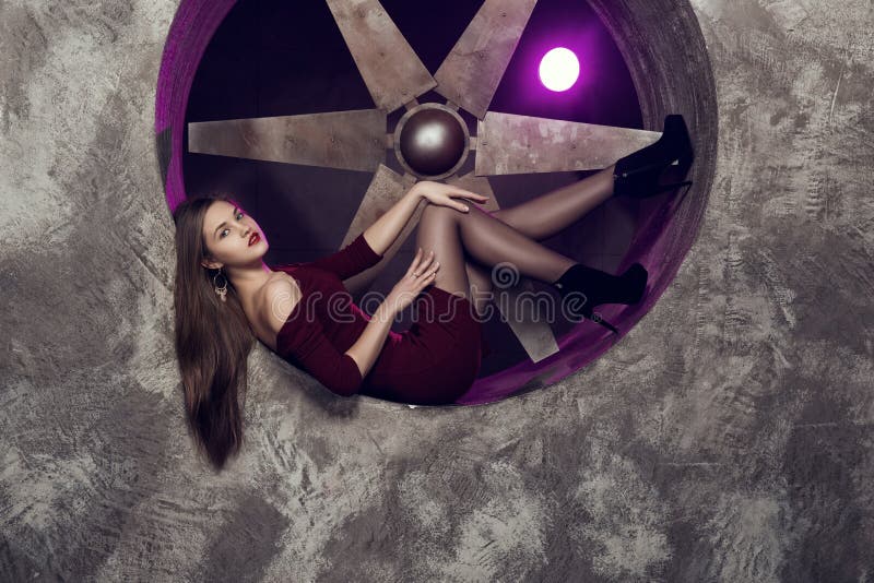 Elegant and beautiful top model near ventilation pipes posing with huge turbo ventilator behind her were lights coming
