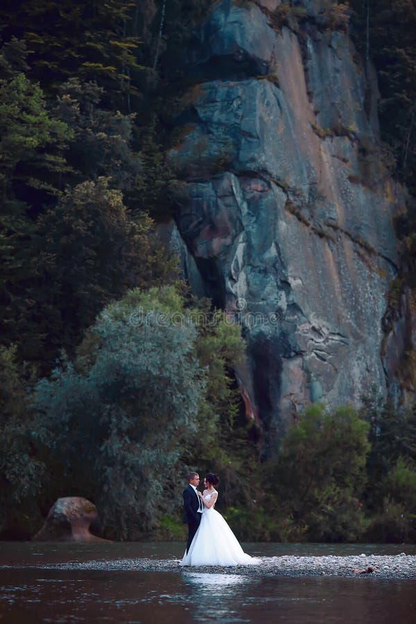 Elegant beautiful wedding couple hugging near blue lake, sensual groom embracing gorgeous bride from behind near river. Wedding da royalty free stock image Elegant beautiful wedding couple hugging near blue lake, sensual groom embracing gorgeous bride from behind near river. Wedding da royalty free stock image