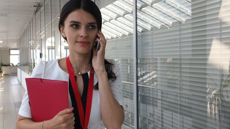 Elegant beautiful woman speaking via smartphone in office building