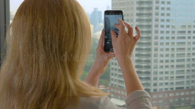 Elegant blonde woman making a photo on the phone. woman photographs the view from the window of the skyscrapers royalty free stock photo Elegant blonde woman making a photo on the phone. woman photographs the view from the window of the skyscrapers royalty free stock photo