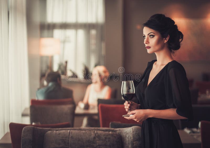 Elegant brunette lady in black evening dress with glass of red w