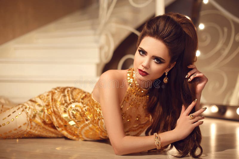 Elegant brunette woman in golden dress lying on the floor b