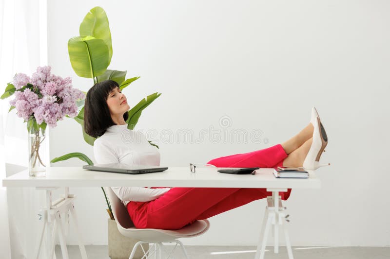 Elegant businesswoman closed eyes with legs on office table with laptop rests during break at work. Relaxed female boss in white shoes on heels sits at the desk, feels stress free. Work life balance.