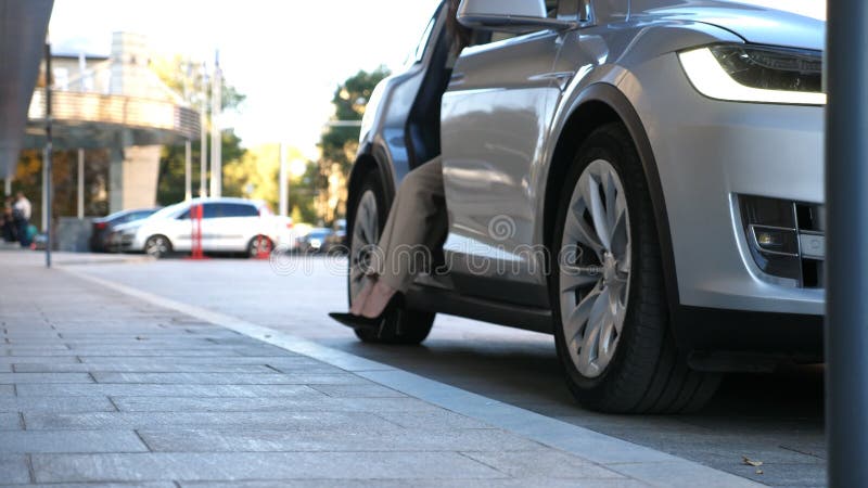 Elegant businesswoman get out from modern car near office building. Young business woman exit from auto and walk to work