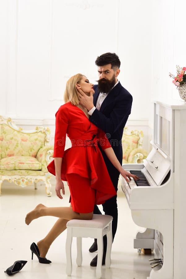 Elegant couple near piano, lady lost her shoe, luxury interior on background. Man in suit touches female face gently