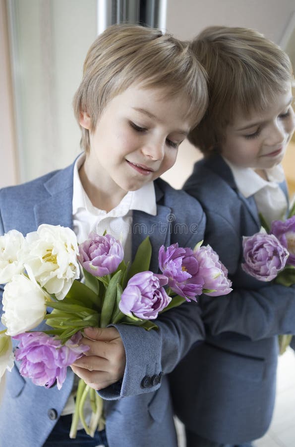 elegant cute stylish boy of 6 years old, a young gentleman, stands near a mirror, holds a bouquet of tulips in his hands