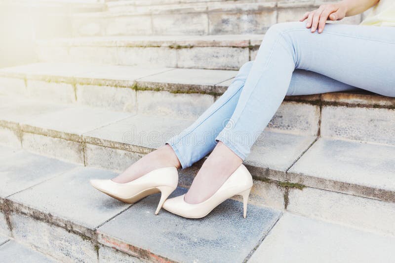 Elegant female legs in blue jeans and beige lacquer shoes on sta