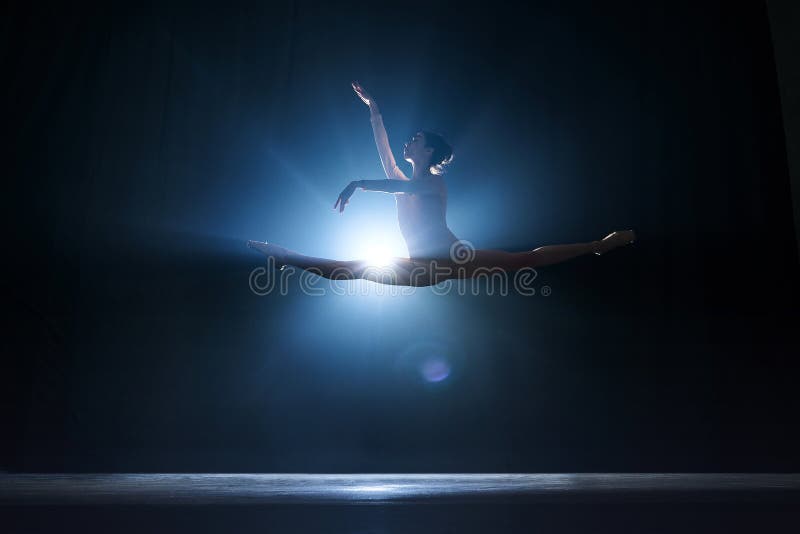 Elegant femininity. Beautiful, tender young woman, ballerina dancing against dark blue background with spotlight