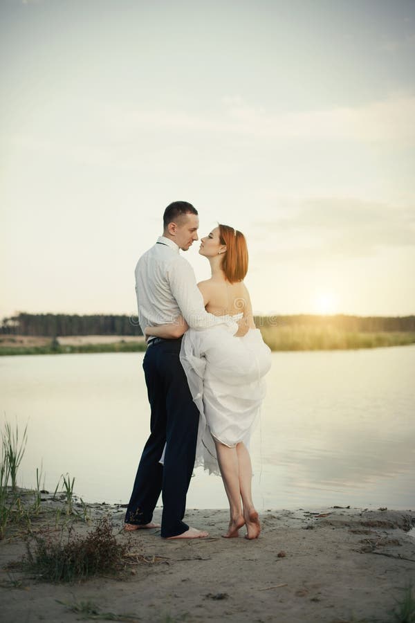 Wedding Couple Sitting On Bridge Near Lake On Sunset At Wedding Day Bride And Groom In Love