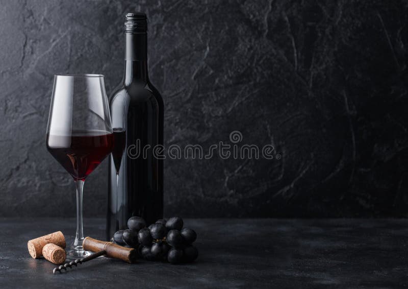 Elegant glass and bottle of red wine with corks and corkscrew on black stone background. Natural Light stock image Elegant glass and bottle of red wine with corks and corkscrew on black stone background. Natural Light stock image