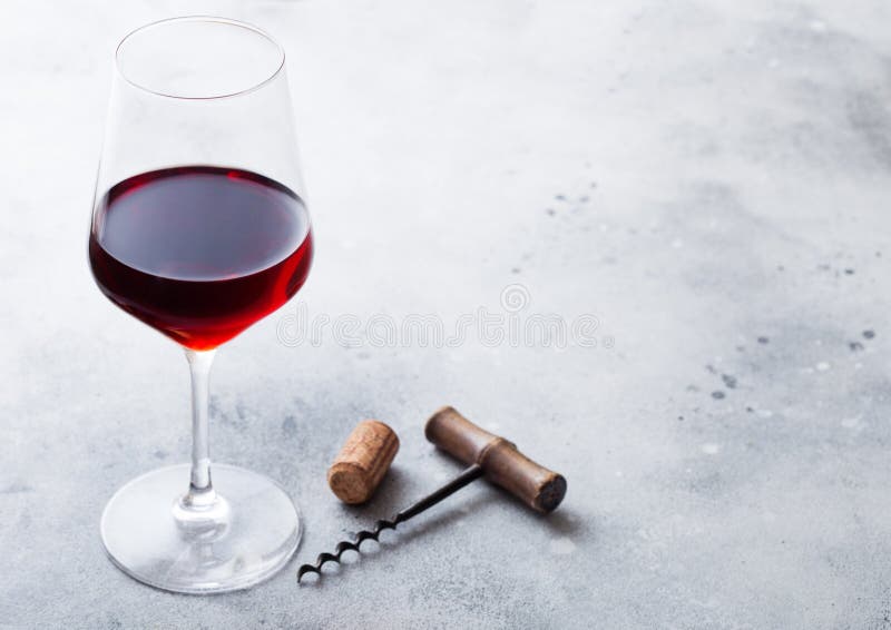 Elegant glass of red wine with cork and opener on stone kitchen table background.