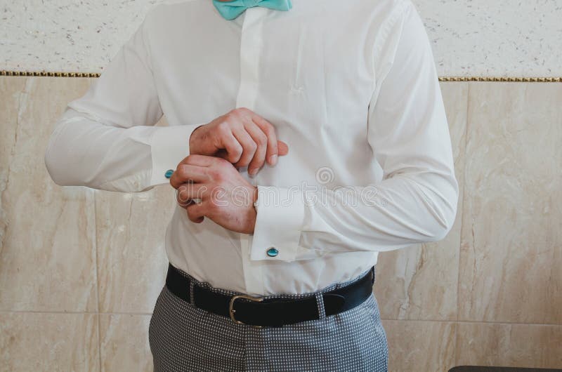 Elegant groom buttons the light blue cufflinks on his white shirt. Tiffany color bow tie. Checkered grey suit and a leather belt. stock photography Elegant groom buttons the light blue cufflinks on his white shirt. Tiffany color bow tie. Checkered grey suit and a leather belt. stock photography