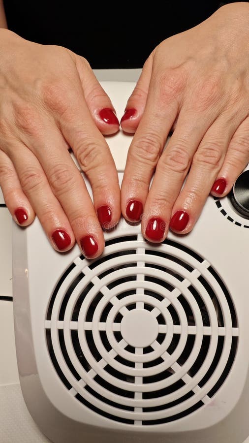 Elegant hands with polished red nails lie atop a sleek nail dryer in a tailored salon environment, highlighting the artistry and care involved in a pampering beauty treatment. Pampering experience stock images, royalty-free photos and pictures