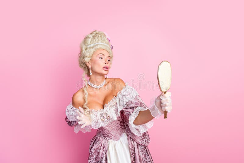 Elegant kvinna i baroque som håller en spegel mot en rosa bakgrund som förmedlar historisk kunglighet och aristokratisk arkivbilder