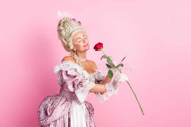 Elegant kvinna i historisk baroque klänning som med röd ros mot en pastellrosa bakgrund royaltyfri bild