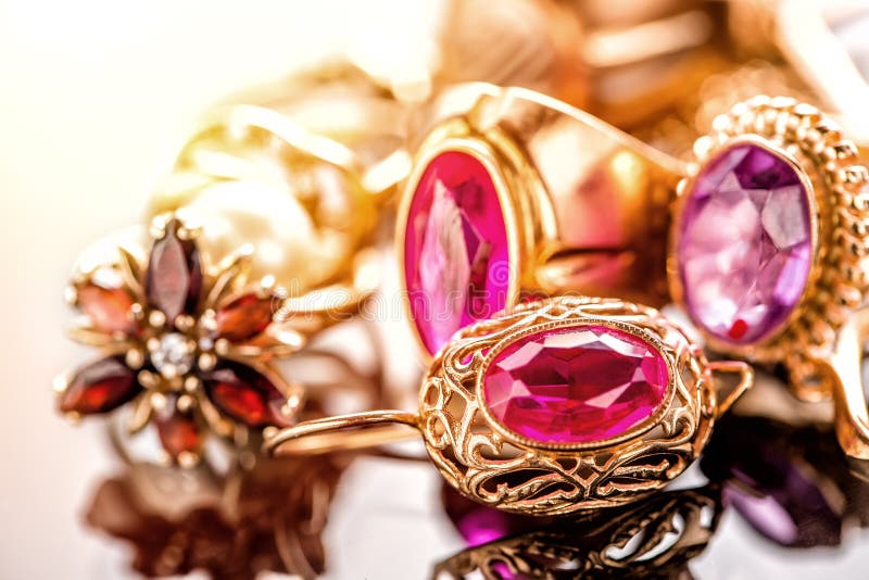 Elegant luxury composition of gold jewelry with ring with red amethyst and ruby gemstone and diamonds on light background close-up