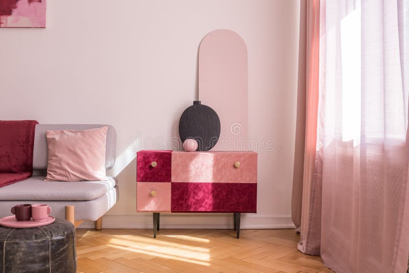 Elegant mockaskinn täckte pastellfärgat rosa, och burgundy färgade kabinettet med guld- handtag bredvid fönster i ljus vardagsrum arkivbilder Elegant mockaskinn täckte pastellfärgat rosa, och burgundy färgade kabinettet med guld- handtag bredvid fönster i ljus vardagsrum arkivbilder