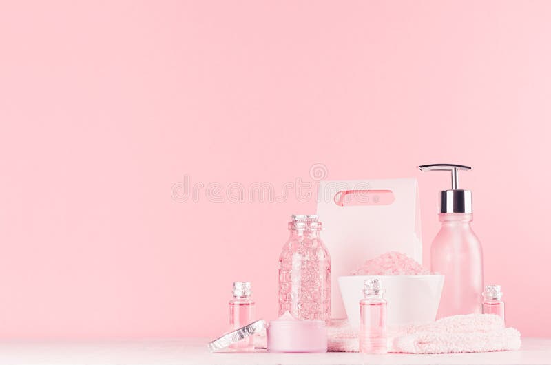 Elegant pink skin and body care products - cream, rose oil, liquid soap, salt, cotton towel and box on white wood table.