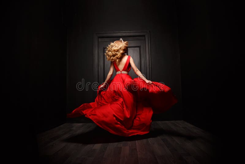 Elegant and woman in the red evening fluttering dress is capture in move, leaving the ceremony the ball, the wooden door is on the background. Indoor. Elegant and woman in the red evening fluttering dress is capture in move, leaving the ceremony the ball, the wooden door is on the background. Indoor