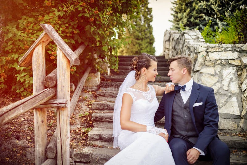 Elegant stylish young bride and groom sitting on the stairs in the park