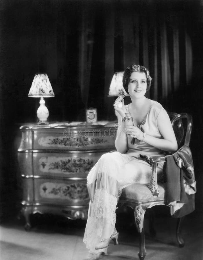 Elegant woman in an evening dress applying perfume to her neck (All persons depicted are no longer living and no estate exists. Supplier grants that there will be no model release issues.)