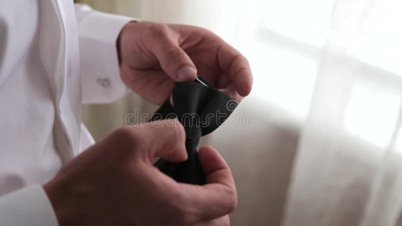 Elegant young fashion man looking at his cufflinks while fixing them