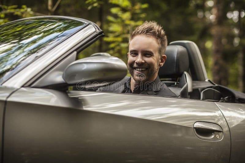 Elegant young happy man in convertible car outdoor.