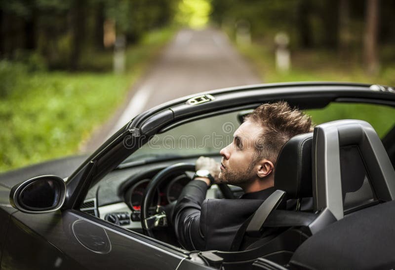 Elegant young happy man in convertible car outdoor.