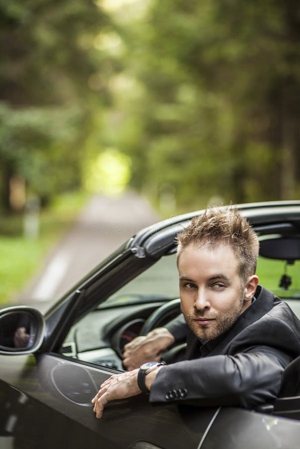 Elegant young happy man in convertible car outdoor.