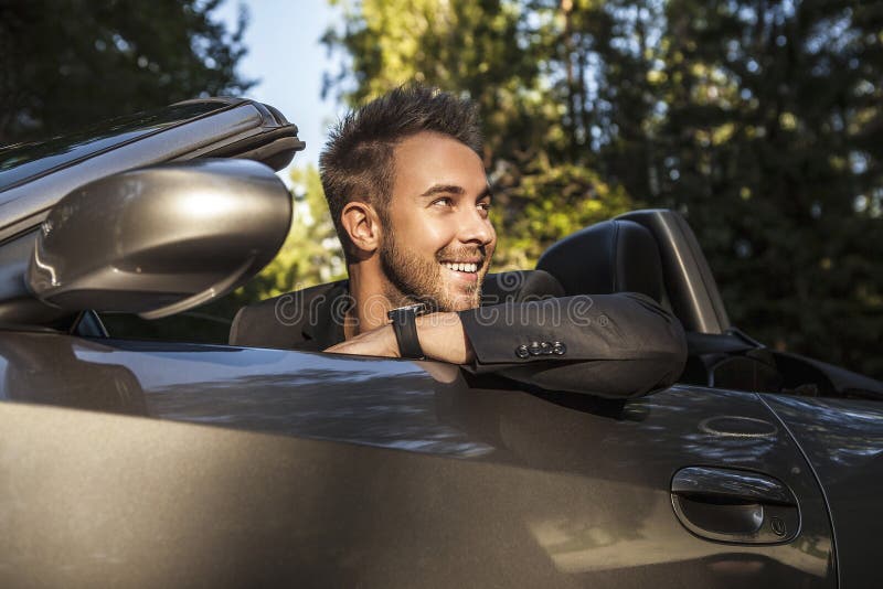 Elegant young happy man in convertible car outdoor.