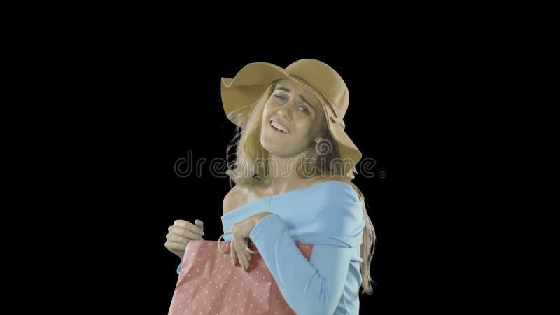Elegant young lady with long hair and freckles on her face in a flesh-colored hat looks into the bag with a gift and