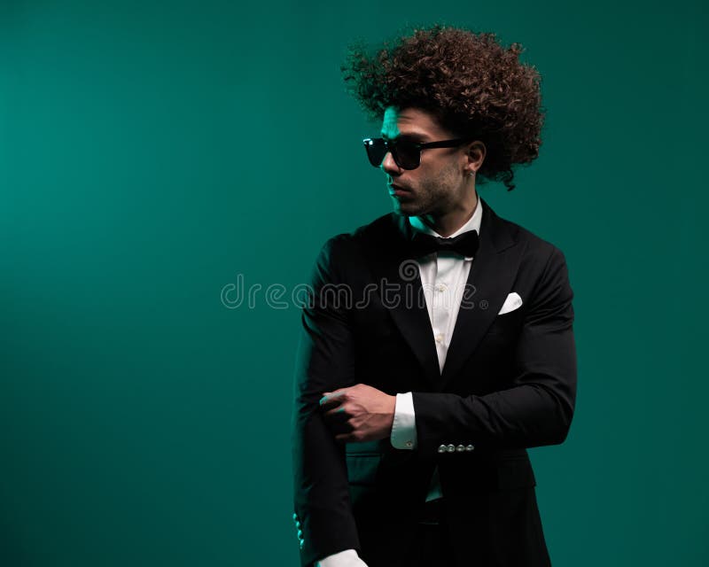 Elegante hombre de confianza en esmoquin negro con gafas de sol ajustando las mangas foto de archivo
