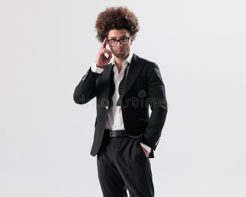 Elegante hombre fresco con pelo rizado ajustando anteojos y sosteniendo la mano en el bolsillo imagen de archivo