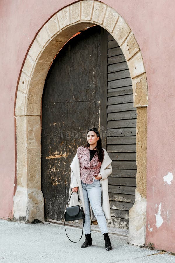 Elegante joven morena mujer de pie delante de un viejo arco puerta de madera de un edificio rojo foto de archivo
