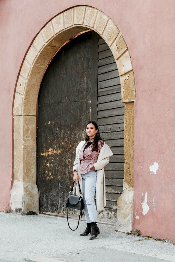 Elegante joven morena mujer de pie delante de un viejo arco puerta de madera de un edificio rojo foto de archivo libre de regalías