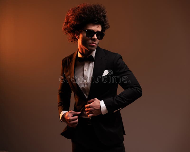 Elegante joven novio con gafas de sol ajustando el esmoquín negro imagenes de archivo