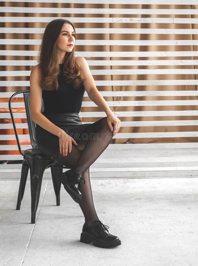Elegante Junge Frau in Schwarzen Kleidern Strumpfhosen Und Stiefel Sitzen  Auf Stuhl Im Studio Hintergrund. Zukunft Und Stockfoto - Bild von ferse,  mann: 228915796