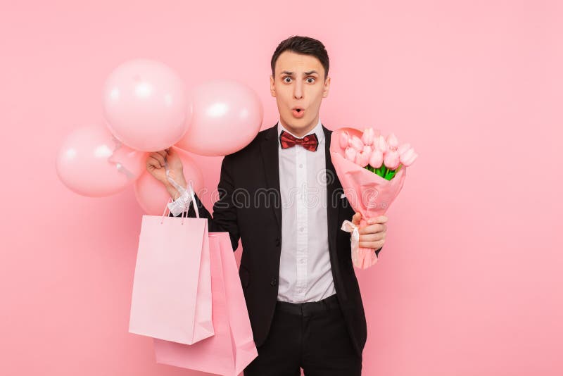 Elegante man, in een kostuum, met een bos van bloemen, zakken en ballons, op een roze achtergrond, het concept de dag van vrouwen stock afbeeldingen Elegante man, in een kostuum, met een bos van bloemen, zakken en ballons, op een roze achtergrond, het concept de dag van vrouwen stock afbeeldingen