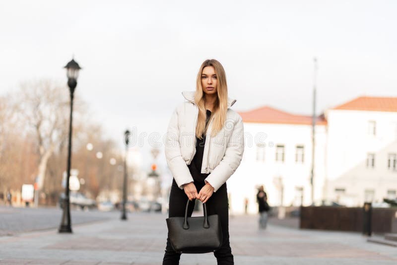 Modelo de una mujer joven con una chaqueta blanca y un bolso de cuero de  moda se encuentra en la ciudad