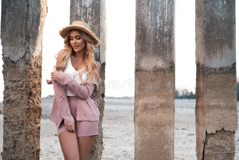 Elegante, moderne und leichte lächelnde junge Frau mit dem langen losen blonden Haar in einem Strohhut genießt ihre Ferien Landsc lizenzfreie stockfotografie