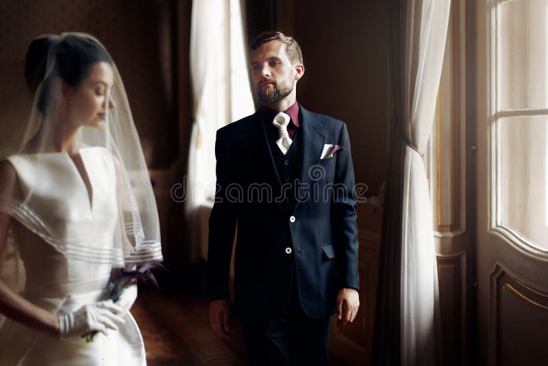 Elegante modieuze knappe bruidegom die schitterende bruid, standi bekijken stock fotografie Elegante modieuze knappe bruidegom die schitterende bruid, standi bekijken stock fotografie
