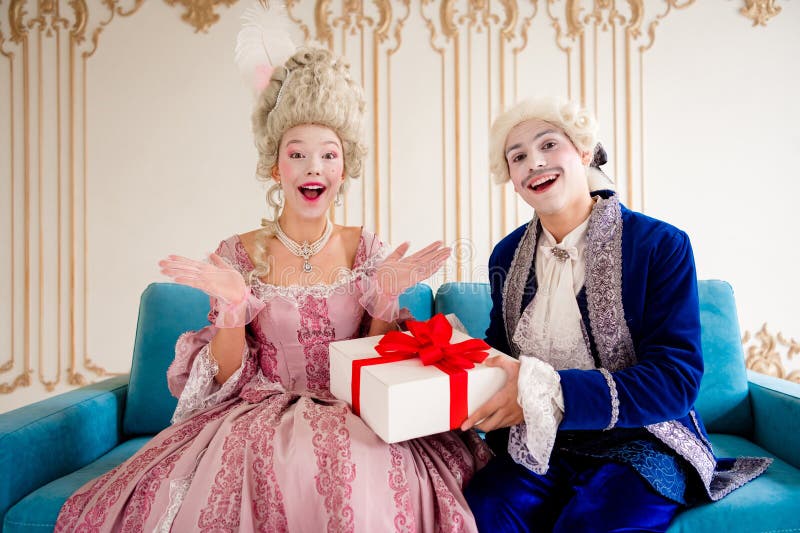 Elegante pareja con trajes barrocos sosteniendo una caja de regalo en un lujoso interior de palacio fotografía de archivo
