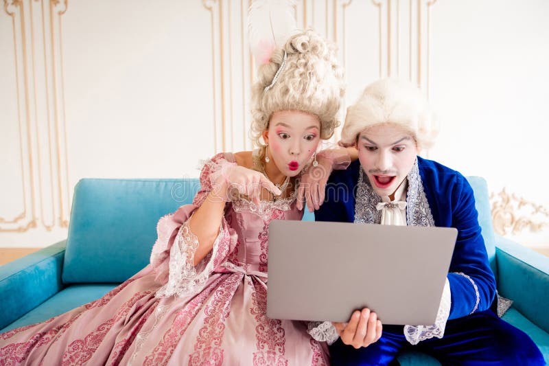 Elegante pareja vestida con atuendo histórico, sorprendida por la tecnología moderna en un lujoso entorno real vintage fotos de archivo libres de regalías