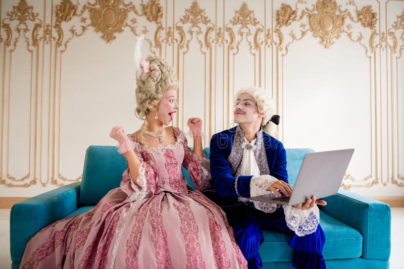 Elegante pareja vestida con trajes históricos que disfrutan del ocio junto con un ordenador portátil en un lujoso interior de pala foto de archivo libre de regalías