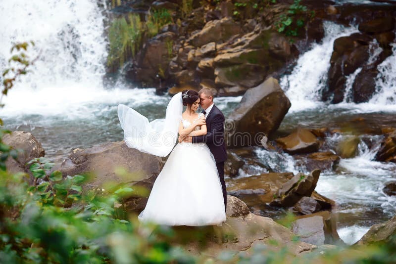 Elegante schöne Hochzeitspaare, die nahe schönem großartigem Wasserfall im Berg aufwerfen Luxuriöses Hochzeitskleid Heiratpaare ü stockfoto Elegante schöne Hochzeitspaare, die nahe schönem großartigem Wasserfall im Berg aufwerfen Luxuriöses Hochzeitskleid Heiratpaare ü stockfoto