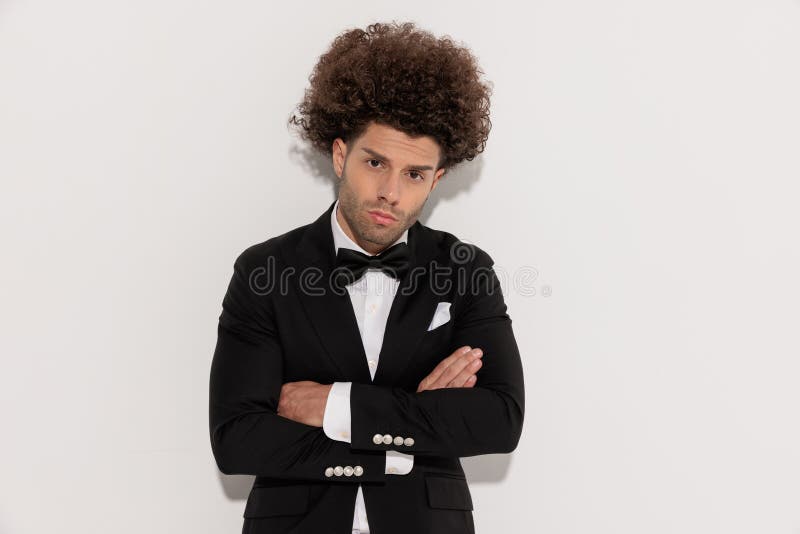 Elegante y atractivo novio con el esmoquin negro cruzando brazos imágenes de archivo libres de regalías