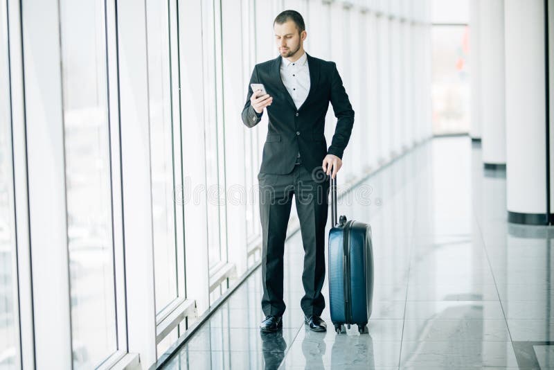 Elegante zakenman die e-mail controleren op mobiele telefoon terwijl het lopen met koffer binnen luchthaventerminal Ervaren manne royalty-vrije stock foto Elegante zakenman die e-mail controleren op mobiele telefoon terwijl het lopen met koffer binnen luchthaventerminal Ervaren manne royalty-vrije stock foto