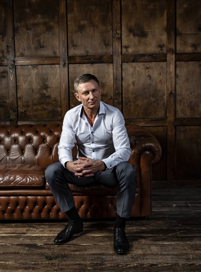 Eleganter moderner Mann in einem Hemd sitzt auf einem ledernen Sofa lizenzfreie stockbilder