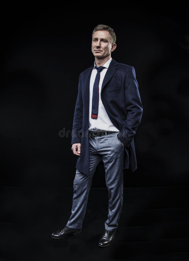 Eleganter moderner Mann in einem Hemd und in einem Mantel auf der Stellung auf einem schwarzen Hintergrund stockbild